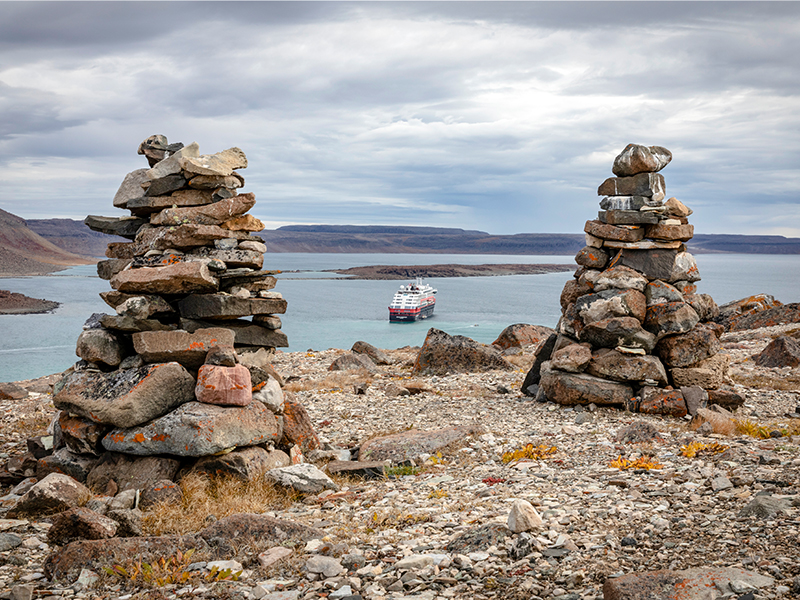 MS Roald Amundsen in the background two cairns built of stones, Ulukhaktok, Canada.